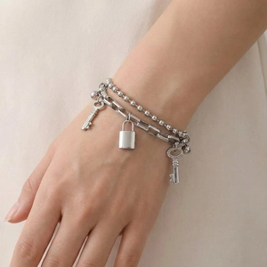 Double-layer silver chain bracelet with padlock and key charms worn on a wrist