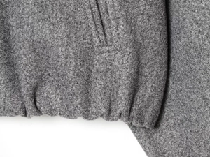 Detail of gray fleece bomber jacket showing pocket stitching and elastic hemline