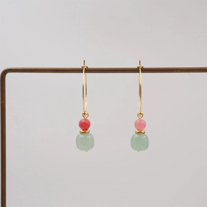 Retro style gold earrings with pink and green beads on a professional metal display stand
