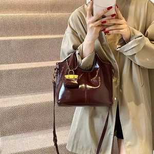 Detail view of glossy oil wax leather tote bag with yellow mini charm and slim strap