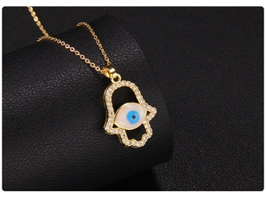 Macro detail of gold Hamsa hand pendant with blue evil eye and sparkling zircon edges