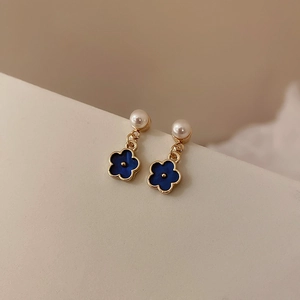 Detailed close-up of blue flower earrings with pearl accents and gold metal finish