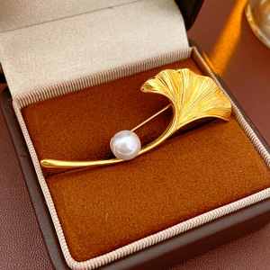 Detailed close-up of a gold-plated ginkgo leaf brooch with a white pearl in a velvet box