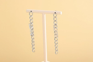 Detail showing long silver chain earrings with cutout LOVE letters on a studio stand
