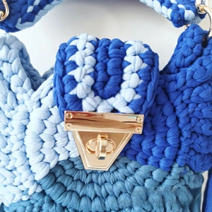 Detail of blue crochet bag featuring textured yarn and golden trapezoid metal twist lock