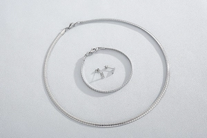 Close-up of silver snake chain necklace and bracelet set with square stud earrings