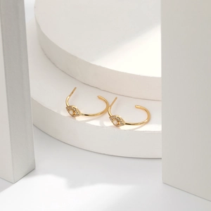 Macro detail of gold C-shaped hoop earrings with blue opal evil eye and white zircons