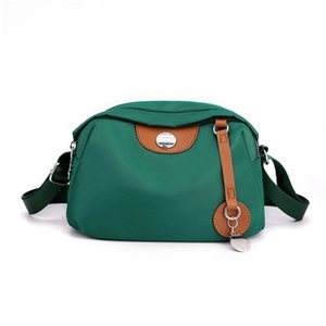 Detail of green nylon crossbody bag with brown leather trim and metal logo emblem