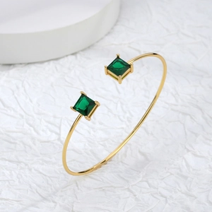 Adjustable gold cuff bracelet featuring two square green zircon stones on a white background