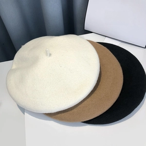 Three wool felt beret hats in cream, camel, and black colors stacked on a white table