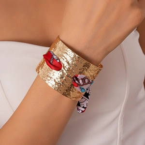 Dettaglio del bracciale rigido dorato martellato con foulard in seta a motivi geometrici