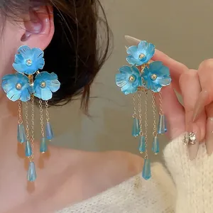 Elegante goldene Quastenohrringe mit blauen Blumen und Kristallanhängern an einem Modell