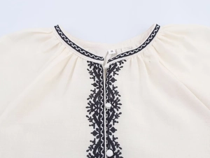 Close-up of ethnic embroidery detail on the neckline of a beige cotton linen shirt