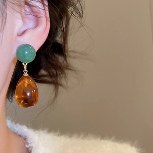 Close-up of green beads and amber resin water-drop pendants on asymmetric earrings
