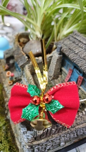 Close-up of a festive red velvet bow with green sequin holly leaves and gold bells