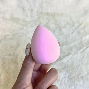 Close-up of a pink teardrop-shaped makeup sponge held against a soft white background