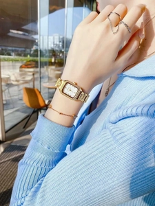 Detail of elegant gold square watch with diamond bezel on model in bright cafe setting