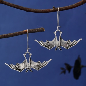 Detail view of retro silver bat earrings hanging on a dry branch for Halloween