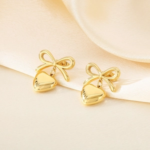Detail view of golden bow and heart stud earrings on elegant silk fabric background