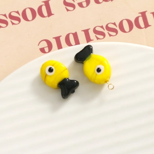 Close-up of cute yellow fish glass beads for DIY jewelry making with gold rings