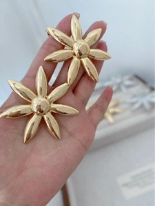 Macro shot of large golden flower earrings held by hand to show premium metallic texture
