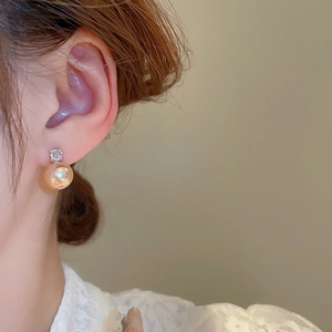 Close-up of elegant champagne gold pearl earrings with sparkling diamond studs on model