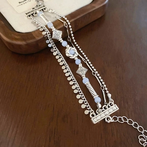 Detail of vintage layered silver bracelet with blue beads and engraved cross metal charm