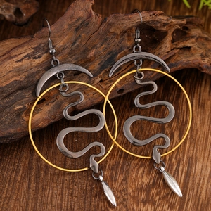 Macro detail of gothic snake earrings with golden moon accent on rustic wood surface