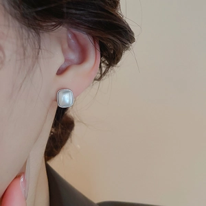 Gros plan d'une boucle d'oreille carrée argentée avec nacre portée par un mannequin