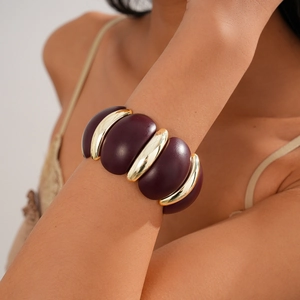 Close-up of wide acrylic geometric bangle in burgundy and gold on model's wrist