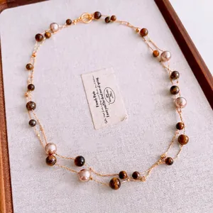 Double-layered tiger eye and pearl necklace with golden beads on a wooden tray