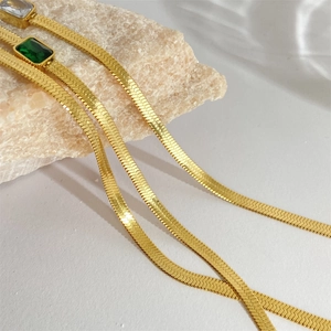 Macro detail of 18k gold plated flat snake chain necklaces with green and clear zircon gems