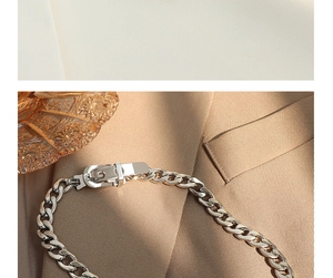 Close-up of silver Cuban chain necklace with a belt buckle clasp on beige fabric