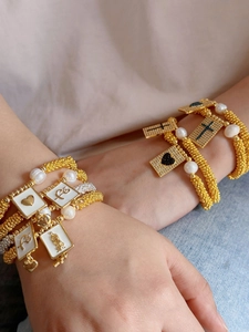 Detail of layered gold charm bracelet with pearls, faith plaque, and religious pendants