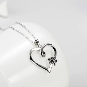 Silver hollow heart necklace with black animal paw print pendant on white ceramic base