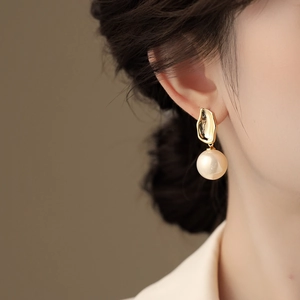 Detail of elegant gold irregular metal earring with hanging pearl worn by model