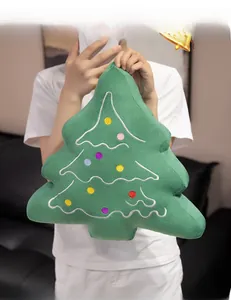 Detailed view of green plush Christmas tree pillow with colorful dot embroidery held by hand