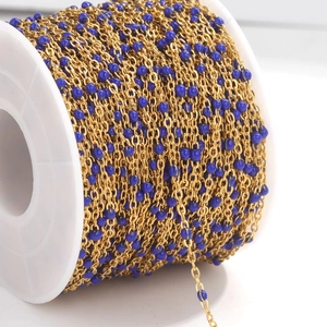 Macro detail of gold stainless steel cross chain with blue enamel beads on a spool
