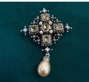 Macro shot of baroque cross brooch with amber stones and teardrop pearl on green velvet