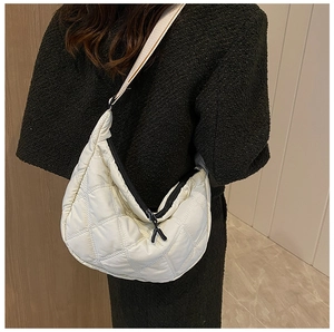 Side view of an ivory quilted crossbody dumpling bag worn over a dark winter coat