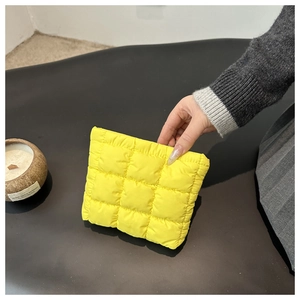 Close-up of yellow quilted nylon pouch with soft puffer square texture held by hand