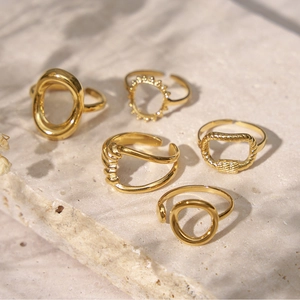 Detailed view of 18K gold plated twisted rings set on a textured beige stone base