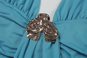 Détail d'une robe plissée bleu canard avec une boucle florale métallique en or rose