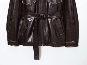 Detailed close-up of dark brown leather jacket with belt, flap pockets and metal zipper