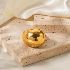Macro di un anello ovale in acciaio dorato su pietra beige con sfondo in seta bianca