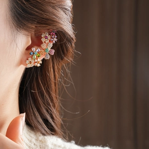 Nahaufnahme einer vergoldeten Ohrmanschette mit bunten Zirkonia-Blumen am Ohr eines Models