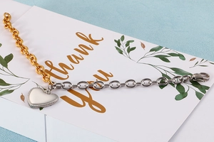 Detail of two-tone gold and silver chain bracelet featuring a heart pendant on a card