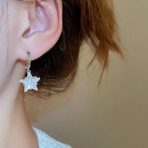 Close-up of sparkling star pendant earrings with zircons on a model's ear