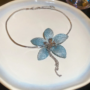 Detail of glitter light blue flower pendant with silver tassels on a sleek snake chain