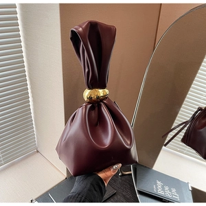 Detail of dark burgundy leather bucket bag featuring a unique knotted handle and gold metal ring